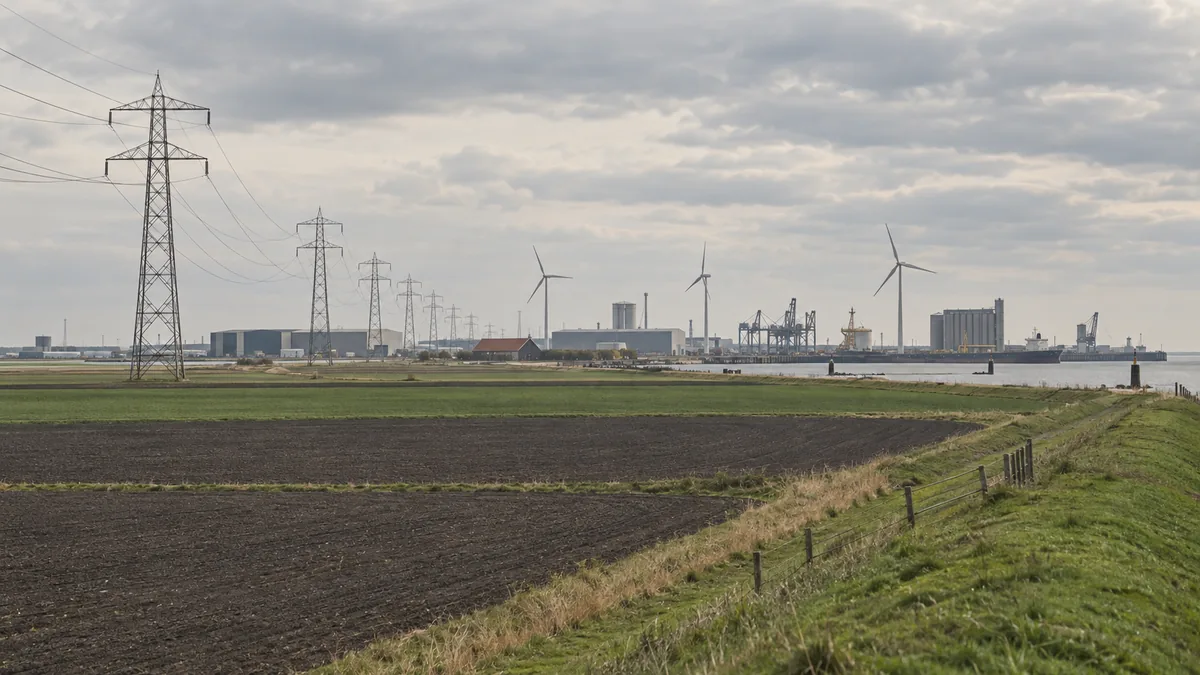 Een algemeen kustlandschap met akkers, een industriehaven en hoogspanningsmasten.