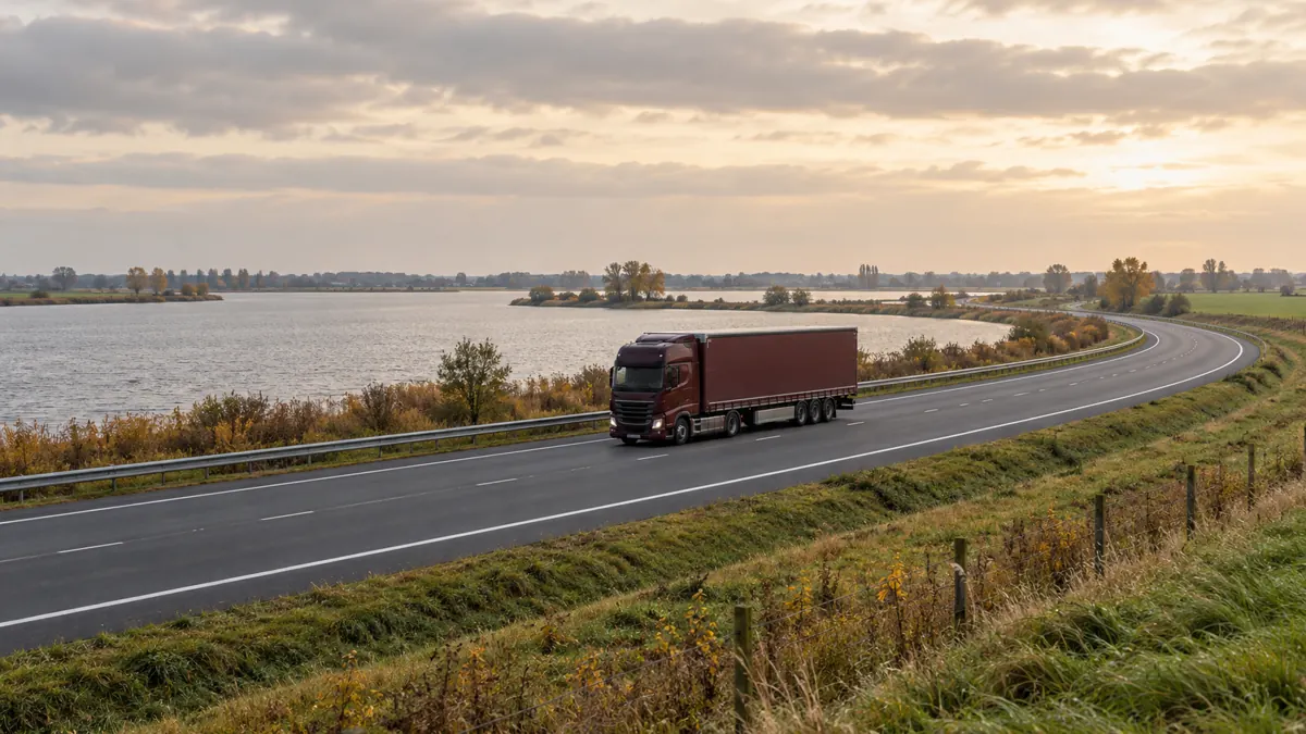 Een vrachtwagen op een weg langs water in een vlak landschap.