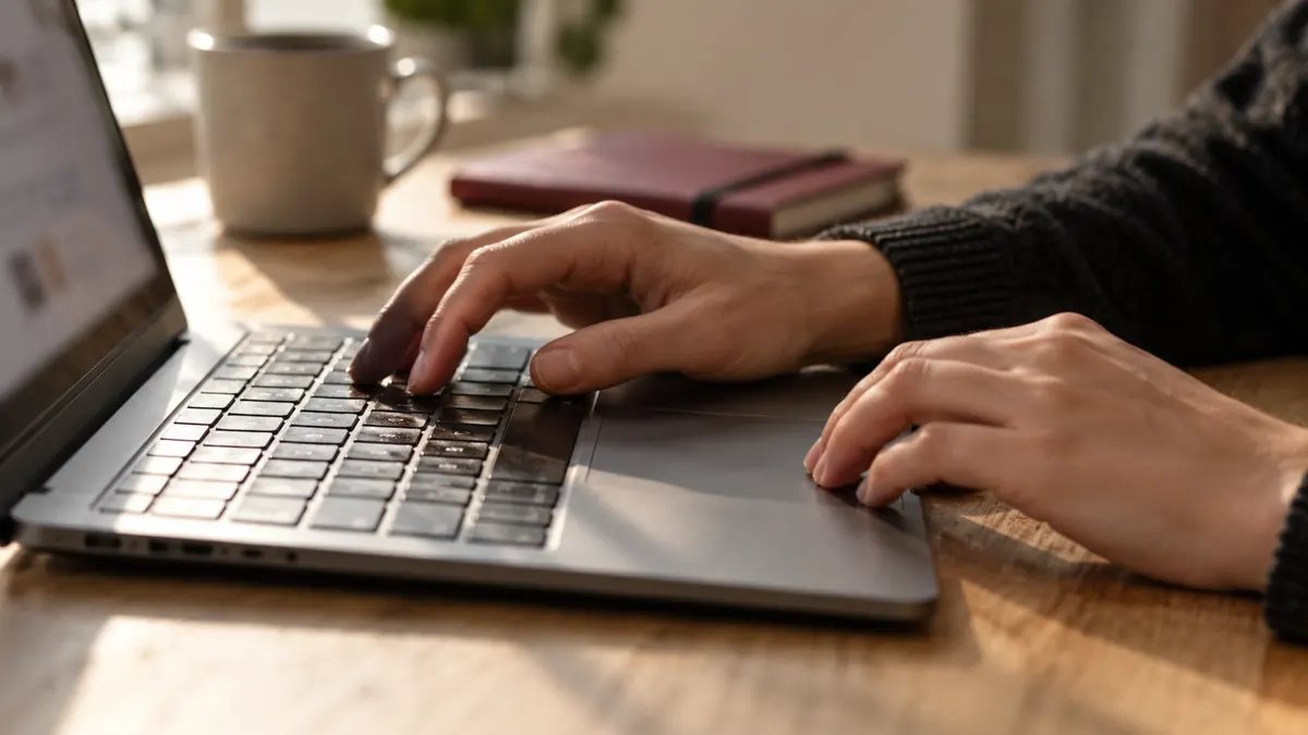 Handen van een onbekende persoon die op een laptop een tekst bewerkt.
